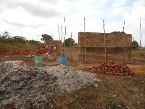 Classrooms rise using bricks made from local soil.